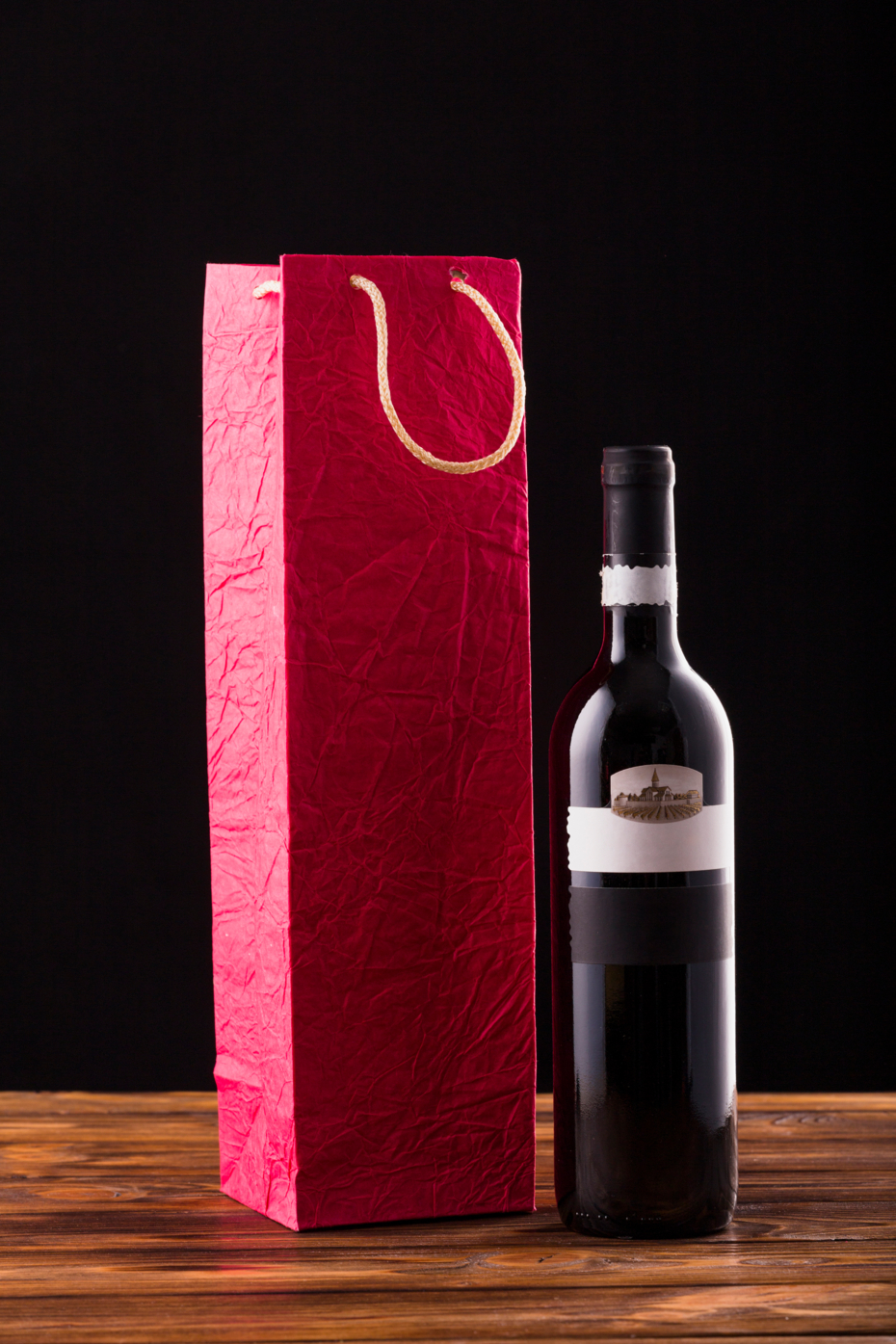 wine-bottle-red-paper-bag-wooden-table-against-black-backdrop