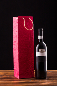 wine-bottle-red-paper-bag-wooden-table-against-black-backdrop